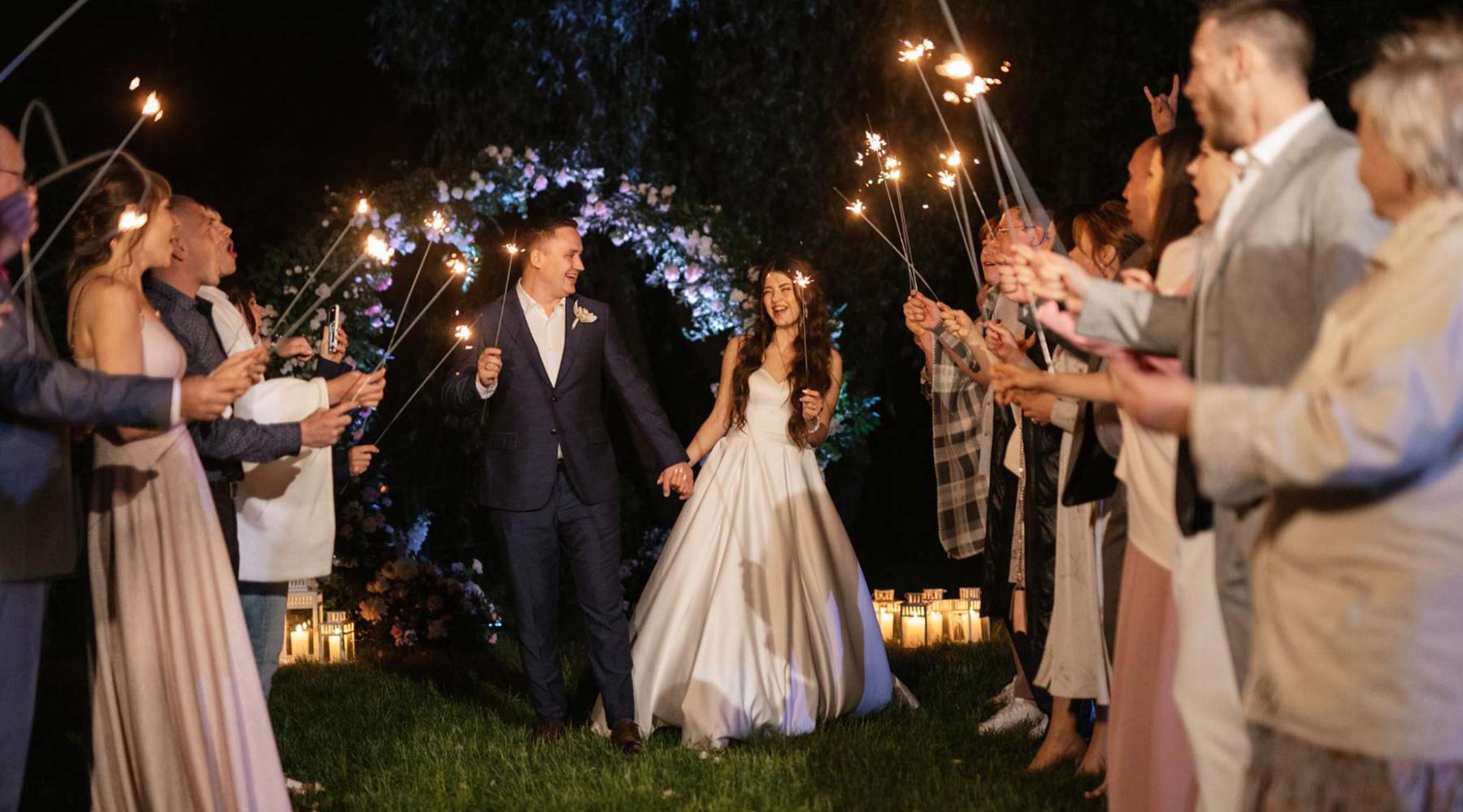 their bridal party at a night wedding. Each member holds a sparkler firework.