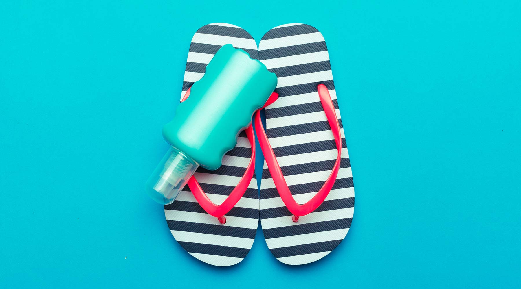 A pair of black and white stripped flip flops sit on a blue background with a bottle of decorative blue flip flop party paint on top.