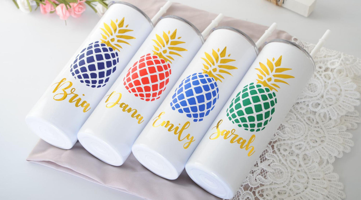 Four white candles with different color pineapples rest on a grey cloth. Each candle has a different name printed below the colorful pineapple..