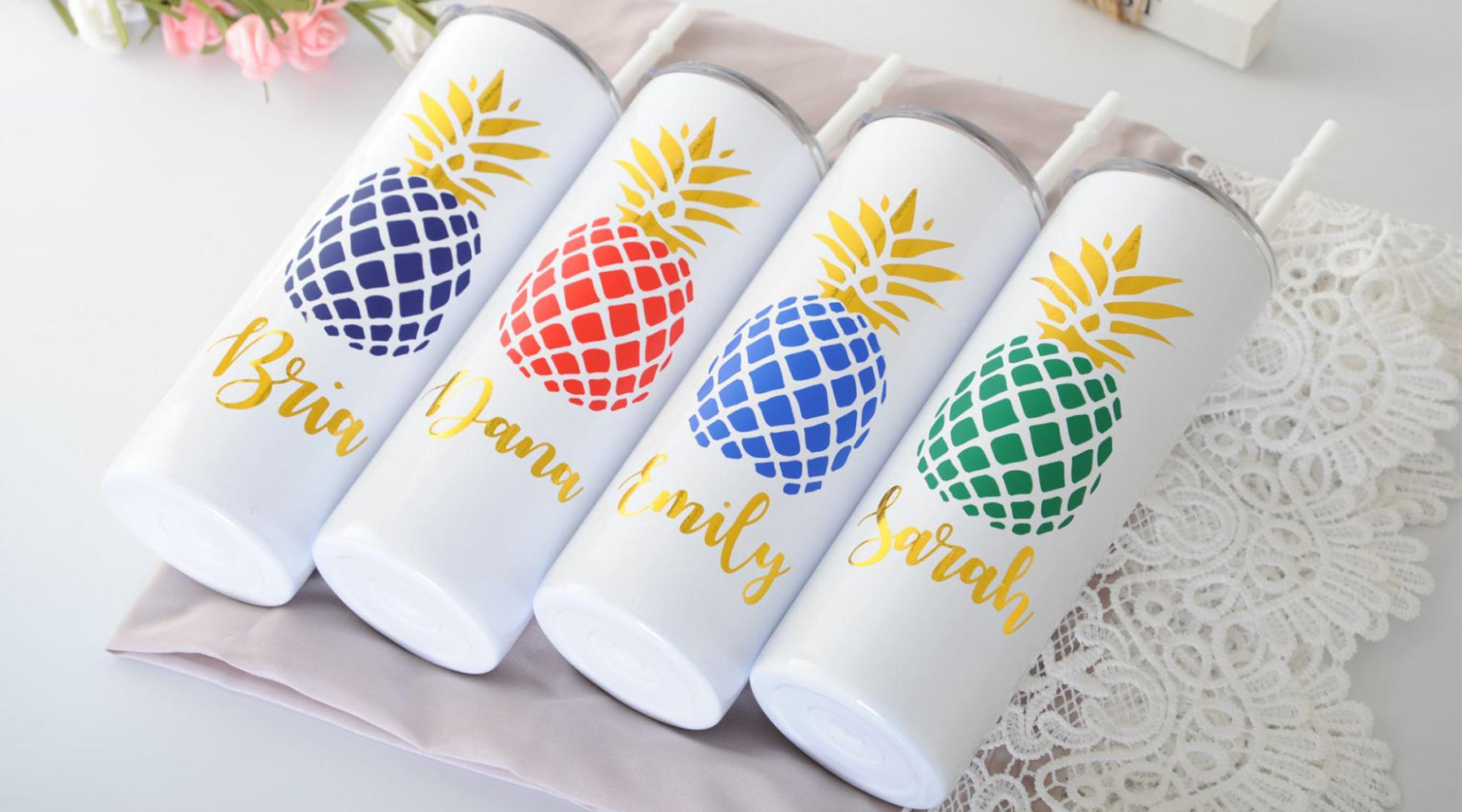 Four white candles with different color pineapples rest on a grey cloth. Each candle has a different name printed below the colorful pineapple..
